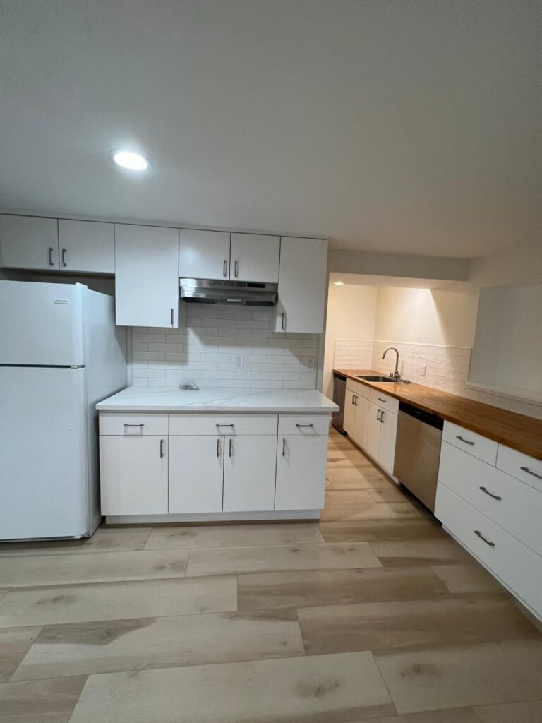 Bright modern kitchen with white cabinets, wood countertops, and a sleek stainless steel dishwasher.