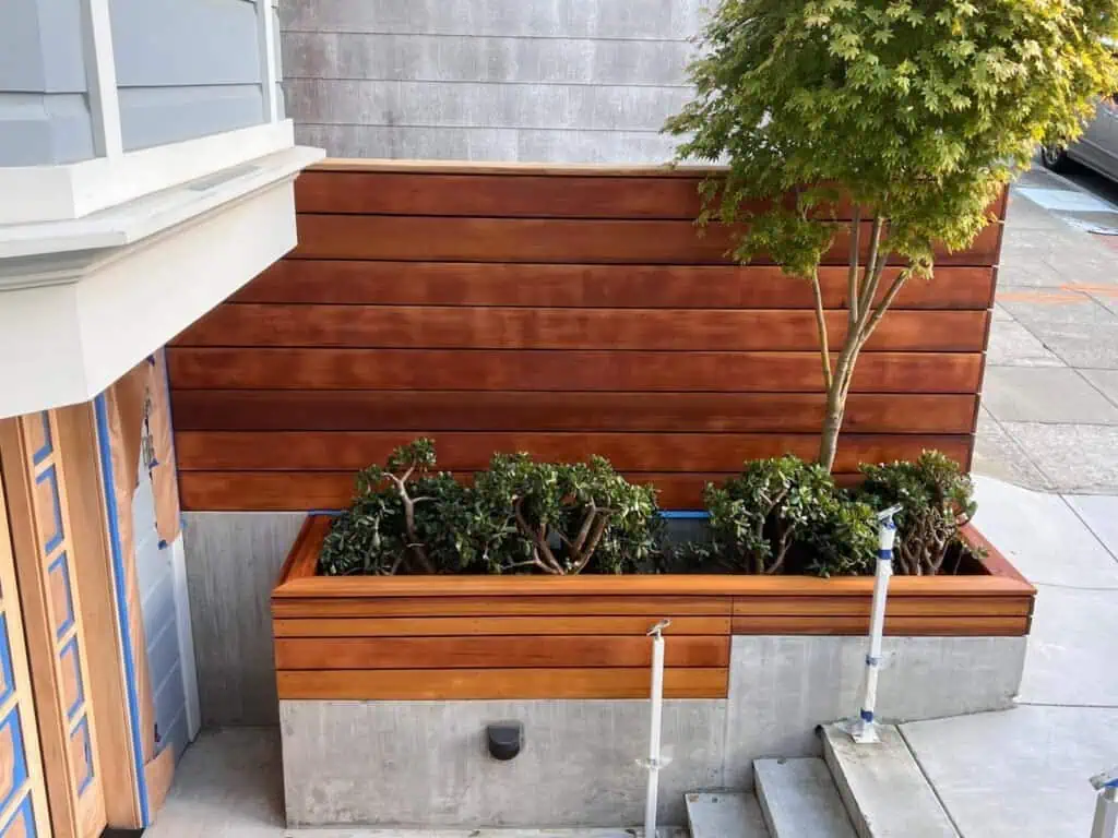 Stylish cedar wood planter box with lush green plants, enhancing modern outdoor aesthetics.